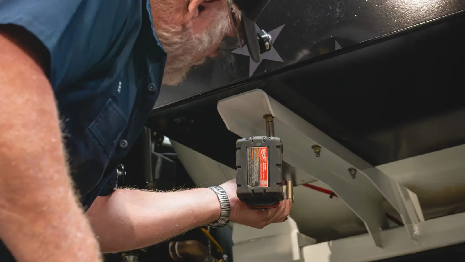 Technician fastening bracket under vacuum tank on Cusco vacuum truck with cordless drill