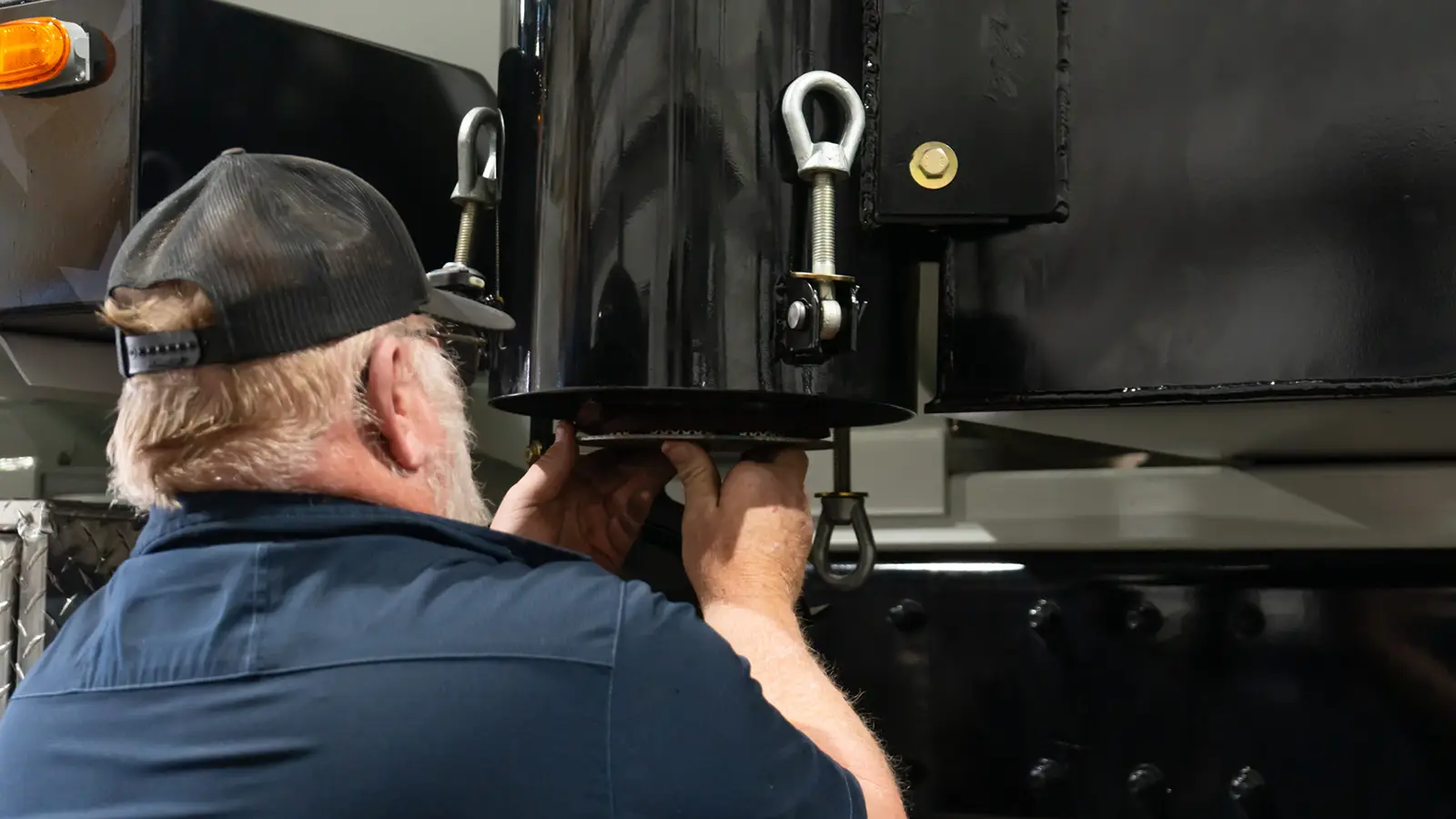 Technician adjusts black tank fittings beneath a Cusco vacuum truck — heavy-duty industrial vacuum equipment assembly.