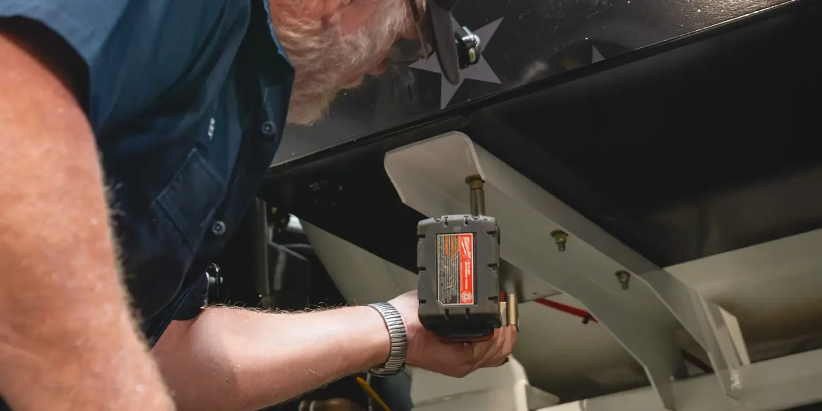 Technician fastening bracket under vacuum tank on Cusco vacuum truck with cordless drill