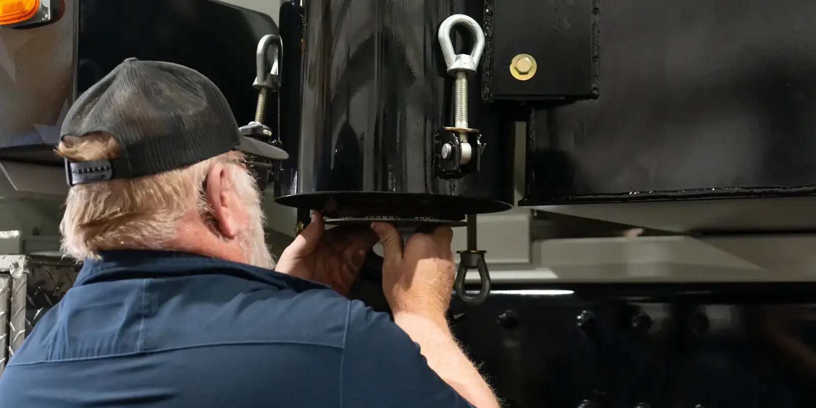 Technician adjusts black tank fittings beneath a Cusco vacuum truck — heavy-duty industrial vacuum equipment assembly.