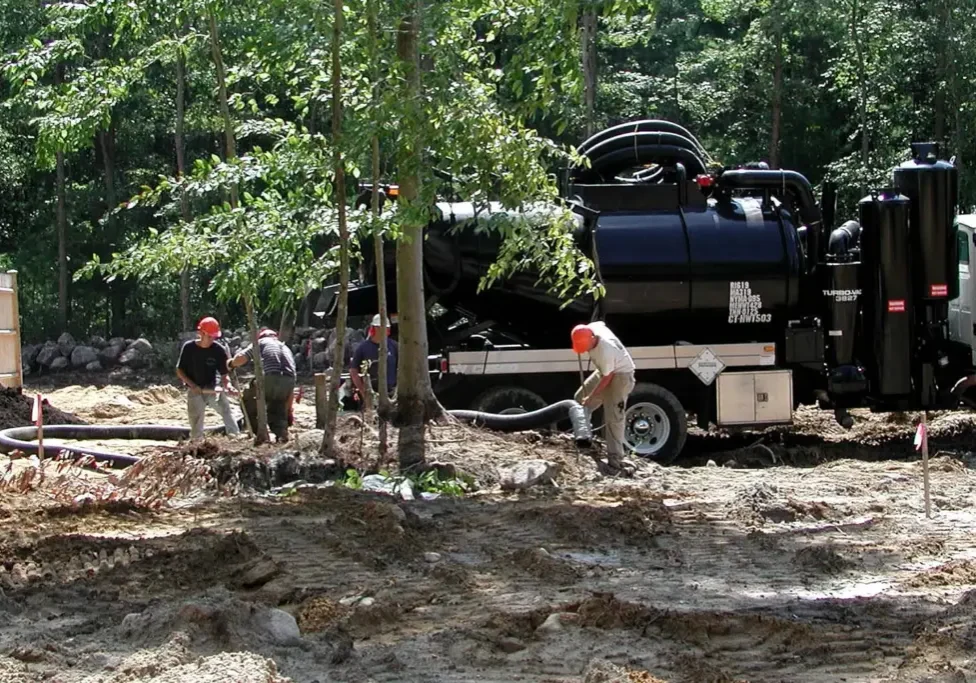 Workers with hoses beside a black heavy-duty vacuum truck at a wooded construction site, Cusco industrial vacuum equipment